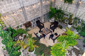 An outdoor seating area with chairs and a fire pit, surrounded by potted plants and greenery.