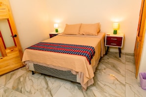 A bed with a patterned blanket, two bedside tables with lamps, a wooden door, and a tiled floor.