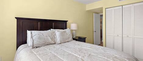 A bed with a dark headboard and multiple pillows, a bedside lamp, and a wardrobe with louvered doors.