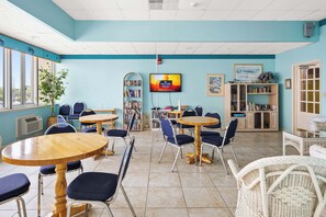 A cafe with round tables and chairs, a television screen, bookshelves, and a window with a view. - Two Bedroom Beachfront Condo with Great Amenities (Ocean City)