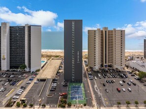 A high-rise building with a prominent vertical sign, adjacent parking lots, and a view of the beach. - Two Bedroom Beachfront Condo with Great Amenities (Ocean City)