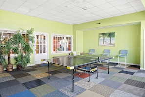 A room with a ping pong table, chairs, a painting, and potted plants. - Two Bedroom Beachfront Condo with Great Amenities (Ocean City)