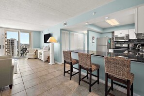 A modern kitchen with a bar area, a dining space, and a view of the city. - Two Bedroom Beachfront Condo with Great Amenities (Ocean City)