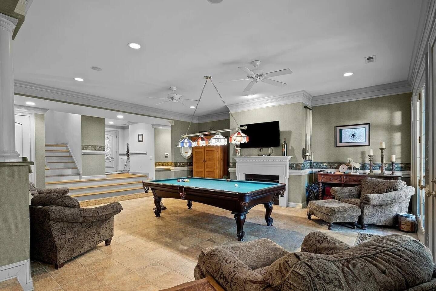 A spacious living room with a pool table, comfortable seating, a fireplace, and a television.