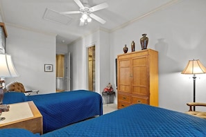 Een hotelkamer met twee bedden, een kledingkast, een bureau en een plafondventilator.