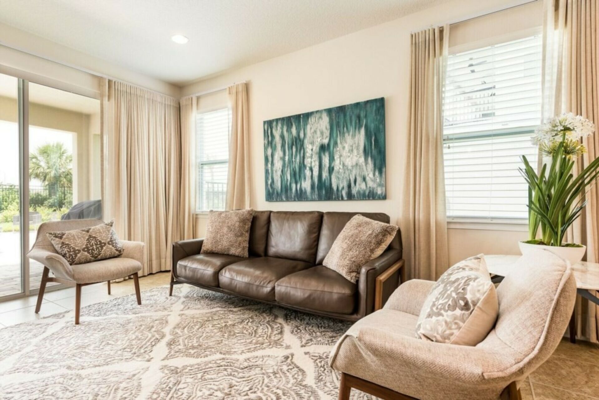 Een woonkamer met een bruine leren bank, beige fauteuils en een vloerkleed met een patroon.