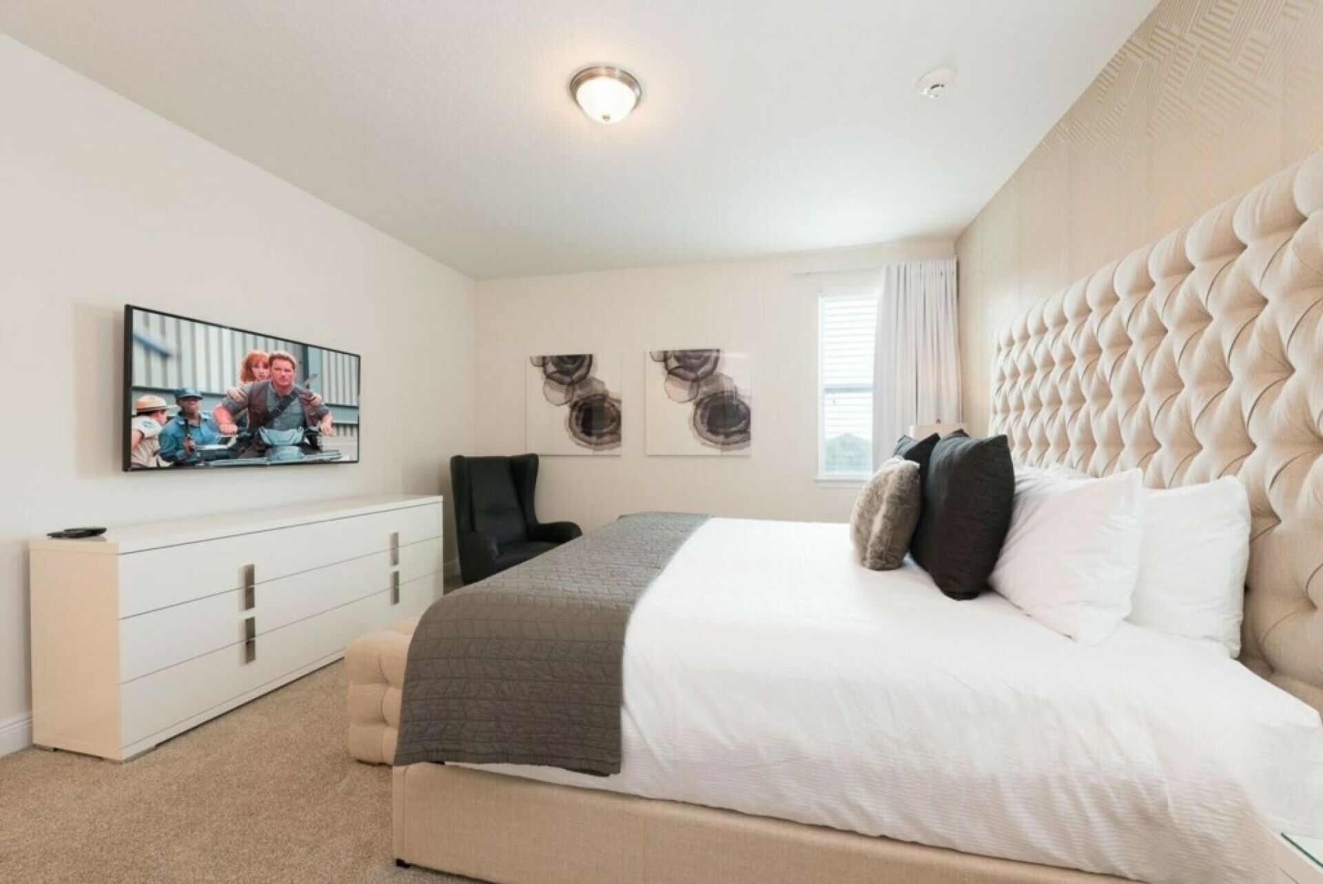 Ein Schlafzimmer mit einem großen Bett, einem an der Wand montierten Fernseher, einem Schreibtisch und einem Sessel.