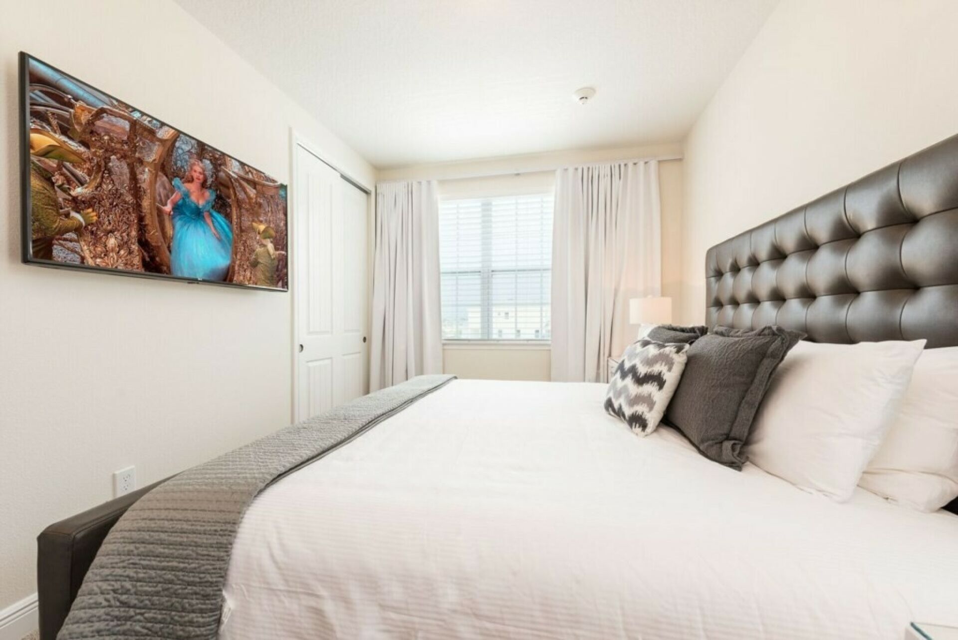 A hotel room with a large bed, a headboard, a painting on the wall, and a window with curtains.