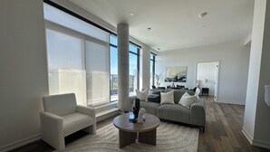 A modern living room with a sofa, armchair, and coffee table, large windows, and a view of the city. - Bright, Spacious 3 Bedroom Penthouse in Vibrant Leslieville in Downtown Toronto (Toronto)