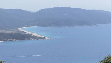 A coastal landscape with a beach, clear blue water, and distant mountains.