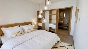Ein Schlafzimmer mit hölzernem Kopfteil, einem großen Bett mit weißer Bettwäsche, einem Nachttisch mit Lampe und einem offenen Kleiderschrank.