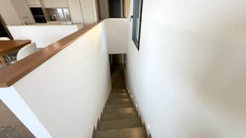Un escalier menant à un espace cuisine au design moderne, avec une rampe en bois et des murs blancs.