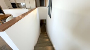 Escadaria que dá acesso a uma cozinha com design moderno, incluindo corrimão de madeira e paredes brancas.