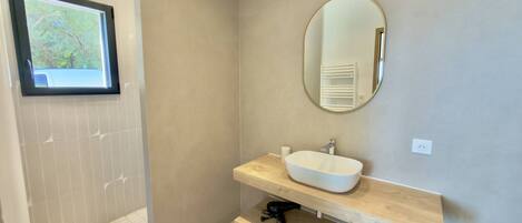 A bathroom with a large mirror, a white sink, and a window with a view of trees.