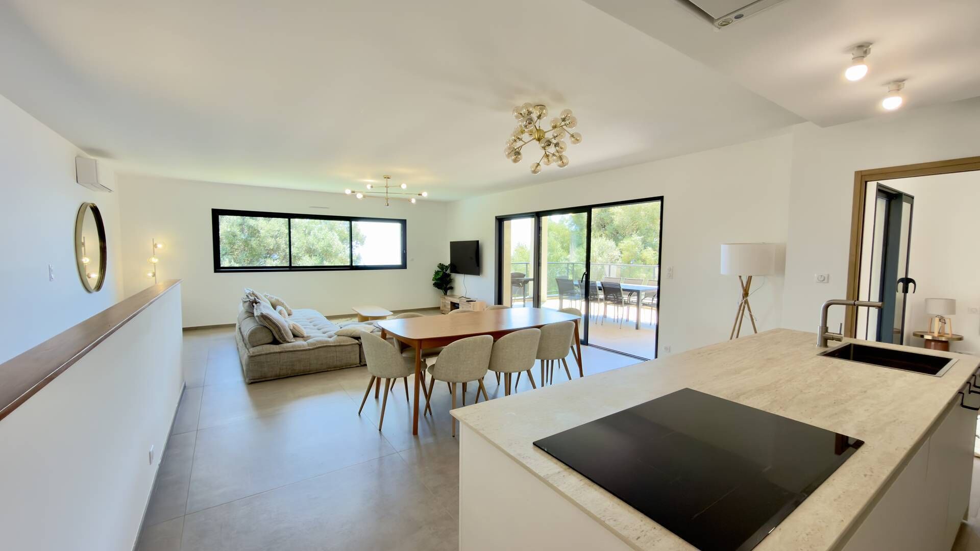 Una cocina moderna con una isla grande, un comedor con mesa y sillas, un sofá y un balcón con mobiliario de exterior.