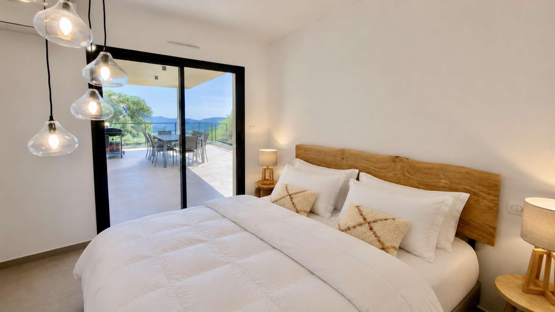 A bedroom with a large bed, two bedside lamps, and a view of an outdoor patio.
