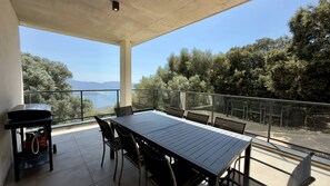 A balcony with a table and chairs, overlooking a scenic view of trees and a body of water. - Villa d'exception avec piscine -  Hauteurs d'Olmeto (OLMETO)