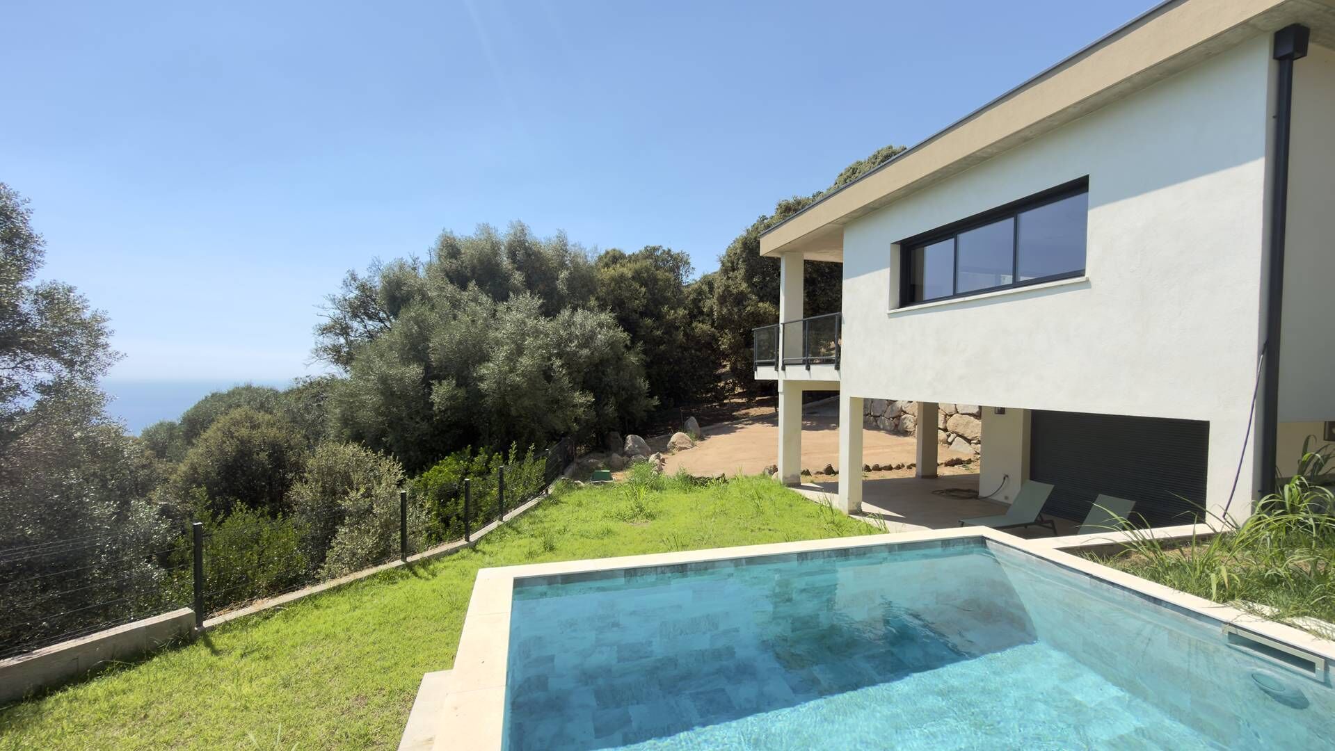 Una casa moderna de dos pisos con piscina, rodeada de vegetación y con vistas a un paisaje montañoso.