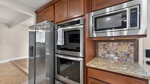 A kitchen with stainless steel appliances, wooden cabinets, and a granite countertop. - Central San Antonio 3BR • PS5 • Sleeps 10 • Blue Yard Homes (San Antonio)