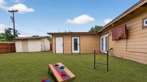 A backyard with artificial grass, a wooden play structure, a small shed, and a door. - Central San Antonio 3BR • PS5 • Sleeps 10 • Blue Yard Homes (San Antonio)