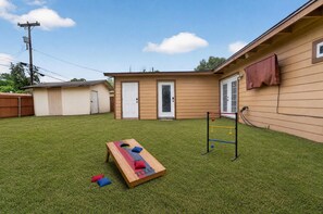 Ein Garten mit Kunstgrasanlage, einer Holz-Spielanlage, einem kleinen Gartenhaus und einer Tür.
