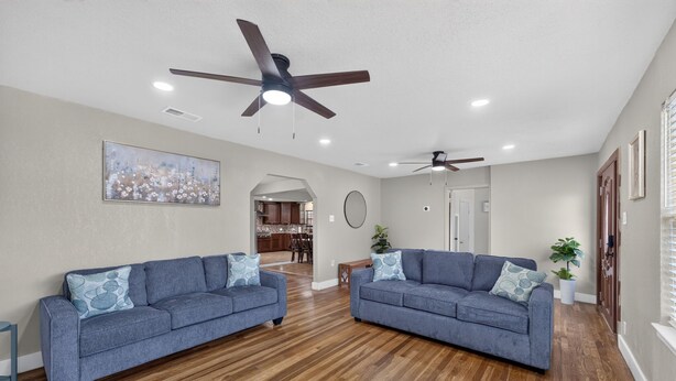 A spacious living room with two sofas, wooden flooring, ceiling fans, recessed lighting, and a view into the kitchen area. - Central San Antonio 3BR • PS5 • Sleeps 10 • Blue Yard Homes (San Antonio)