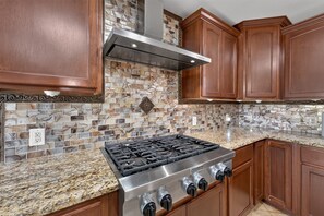 A kitchen with a stainless steel stove, wooden cabinets, and a mosaic tile backsplash. - Central San Antonio 3BR • PS5 • Sleeps 10 • Blue Yard Homes (San Antonio)