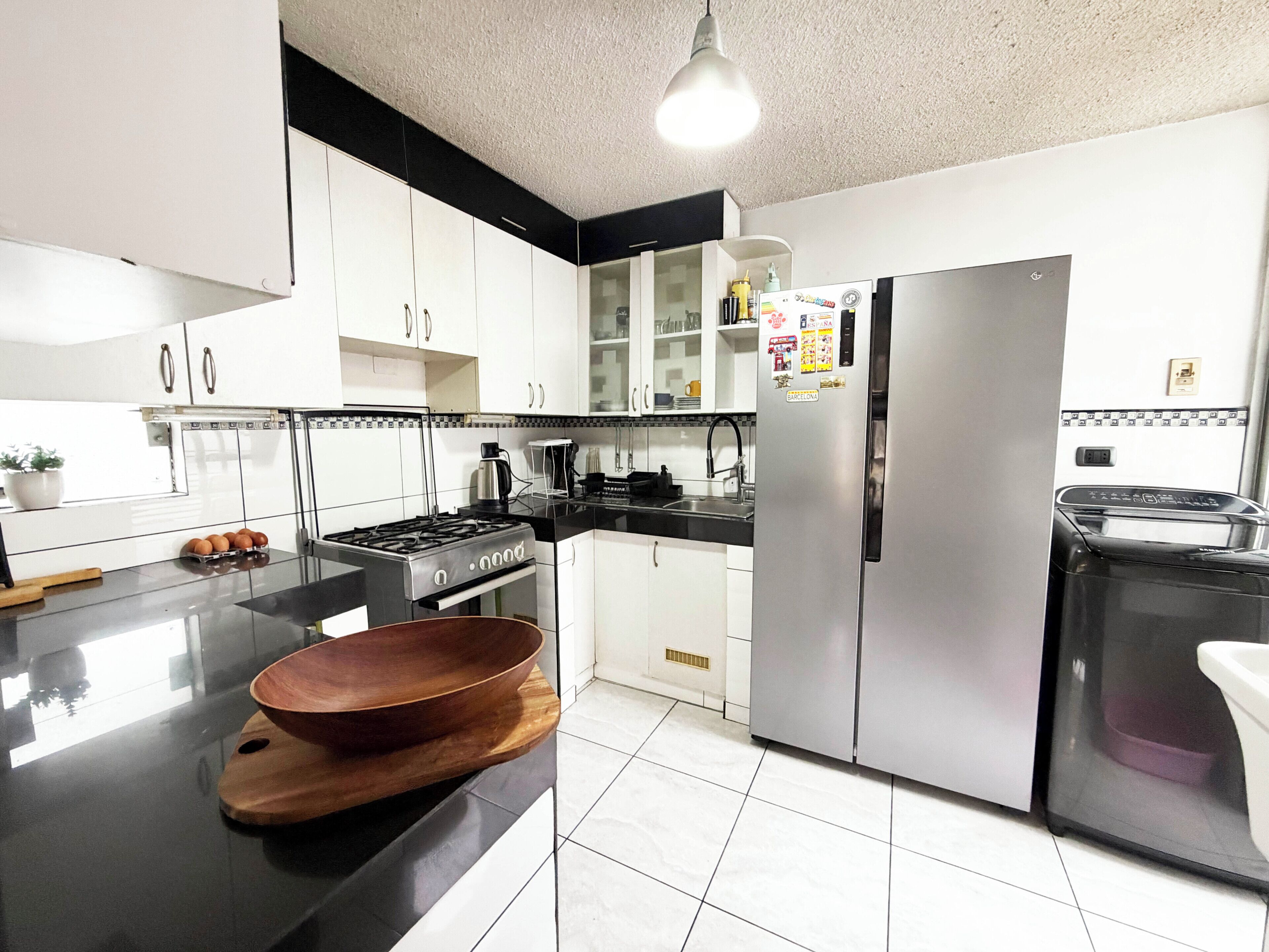 A modern kitchen with white cabinets, a stainless steel refrigerator, a wooden bowl on a cutting board, and a gas stove.