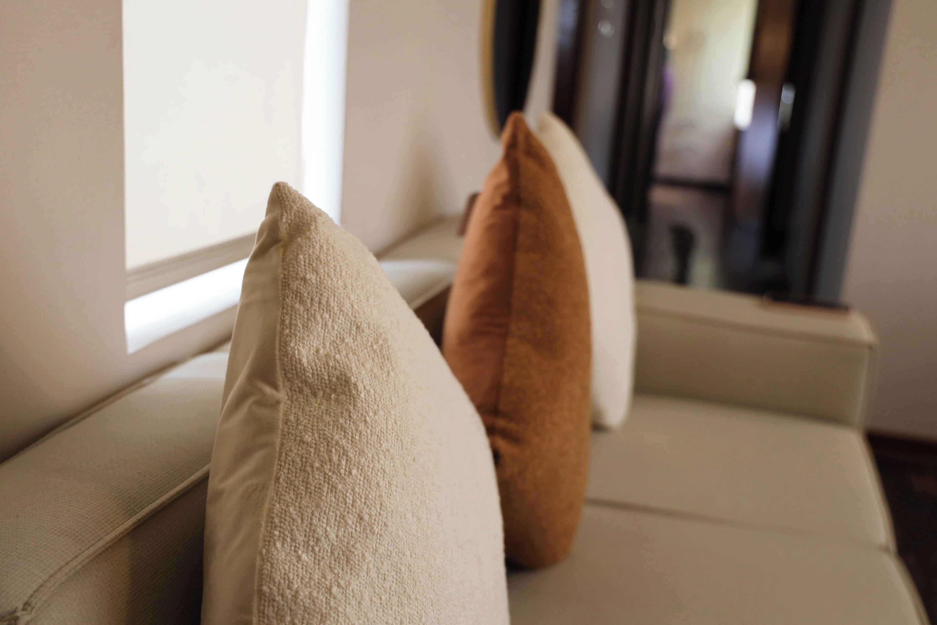 A sofa with two pillows, one beige and one brown, positioned near a window.
