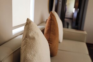 Un sofá con dos almohadas, una beige y otra marrón, cerca de una ventana.