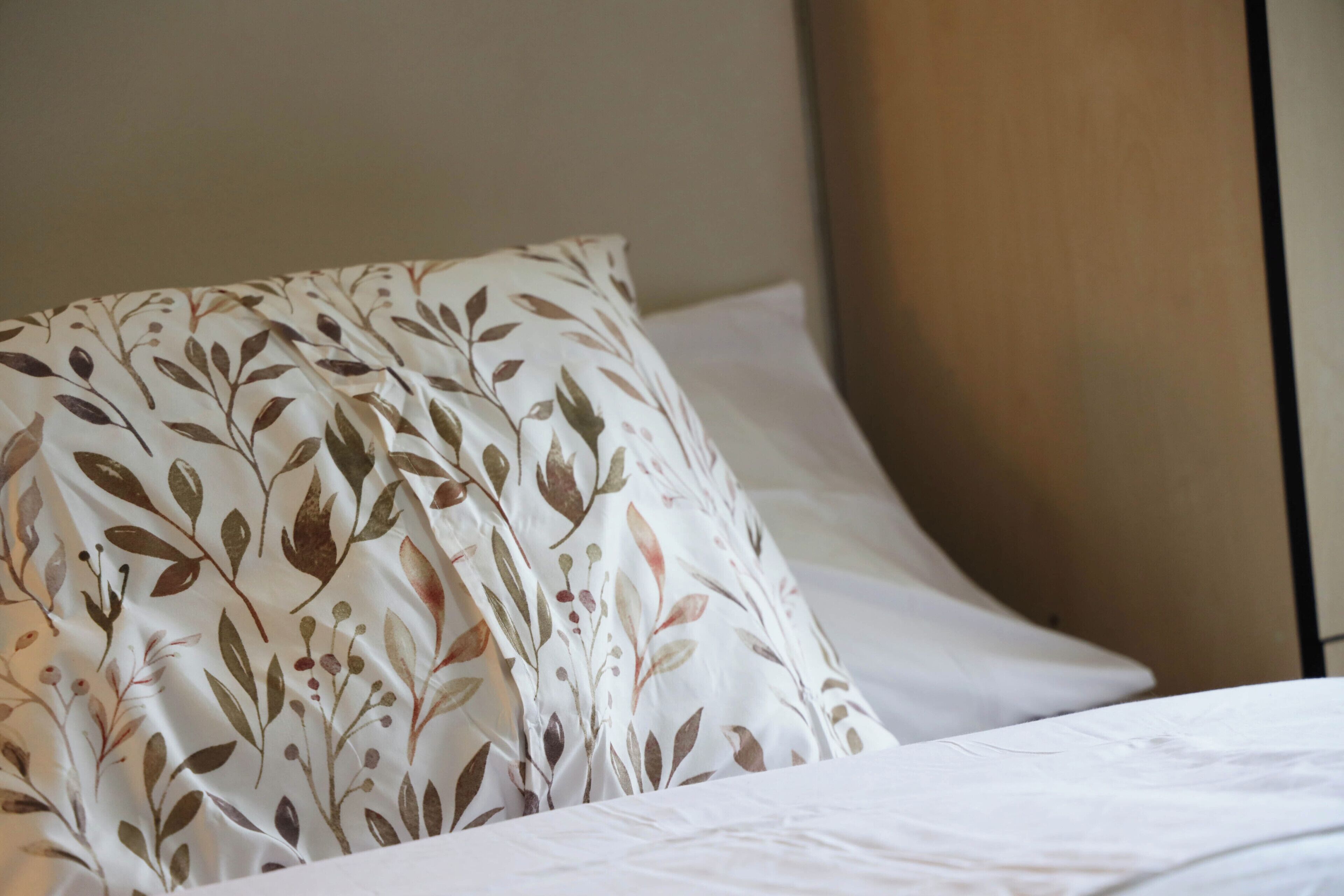 A bed with a white sheet and a pillow with a leaf pattern.