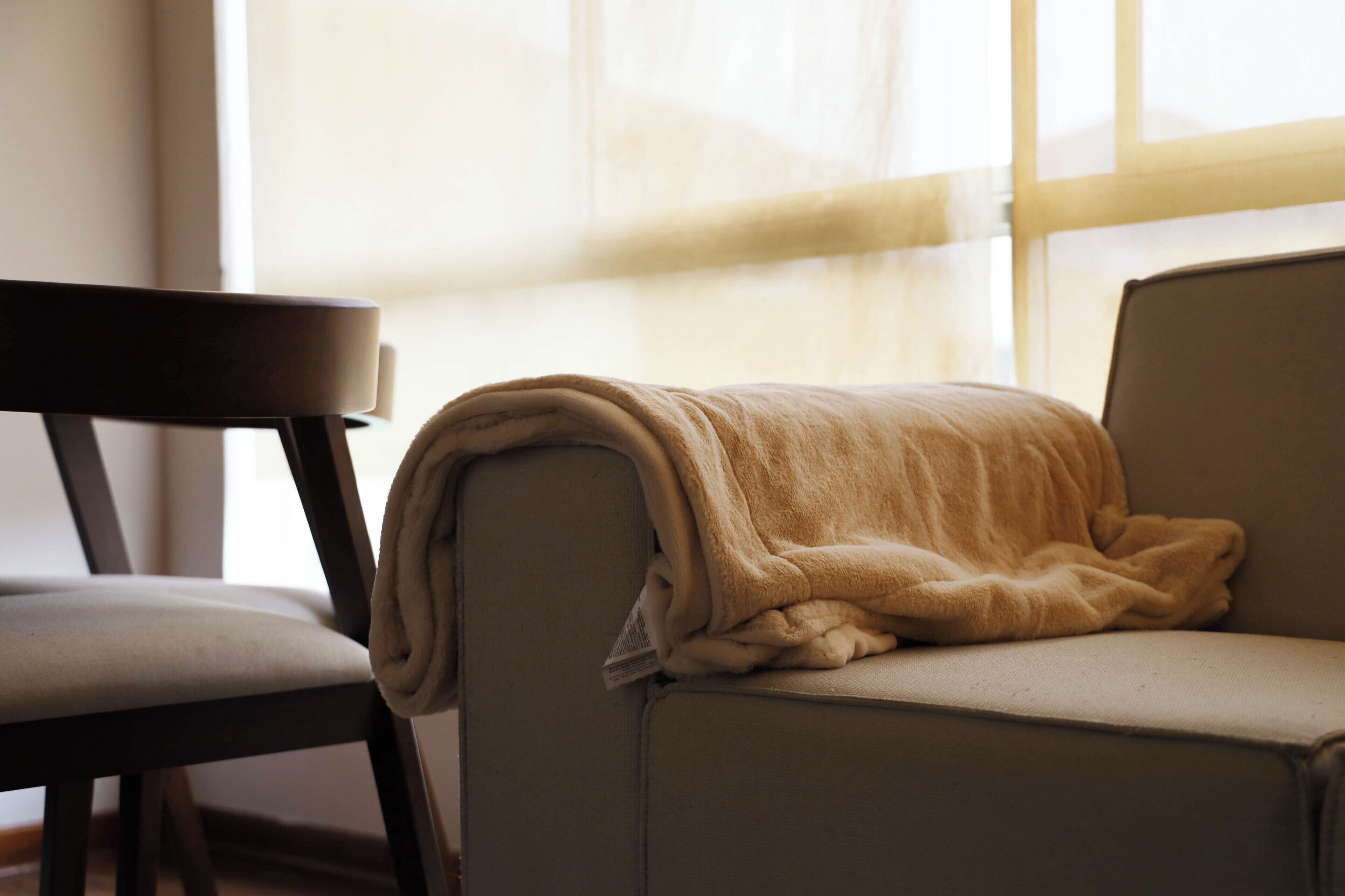 A chair and a sofa with a blanket on the sofa.