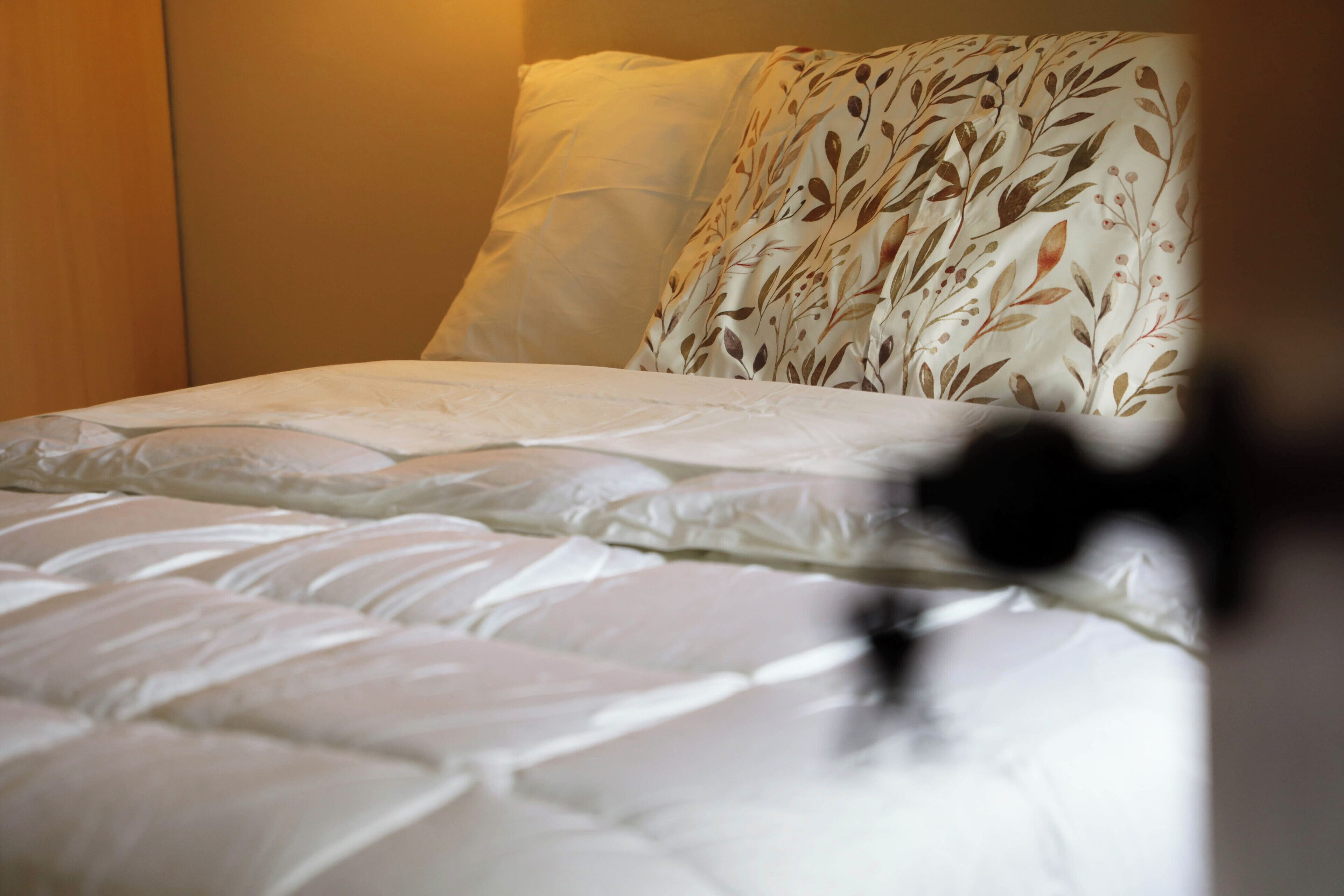 Una cama con edredón blanco y almohada estampada con motivos florales.