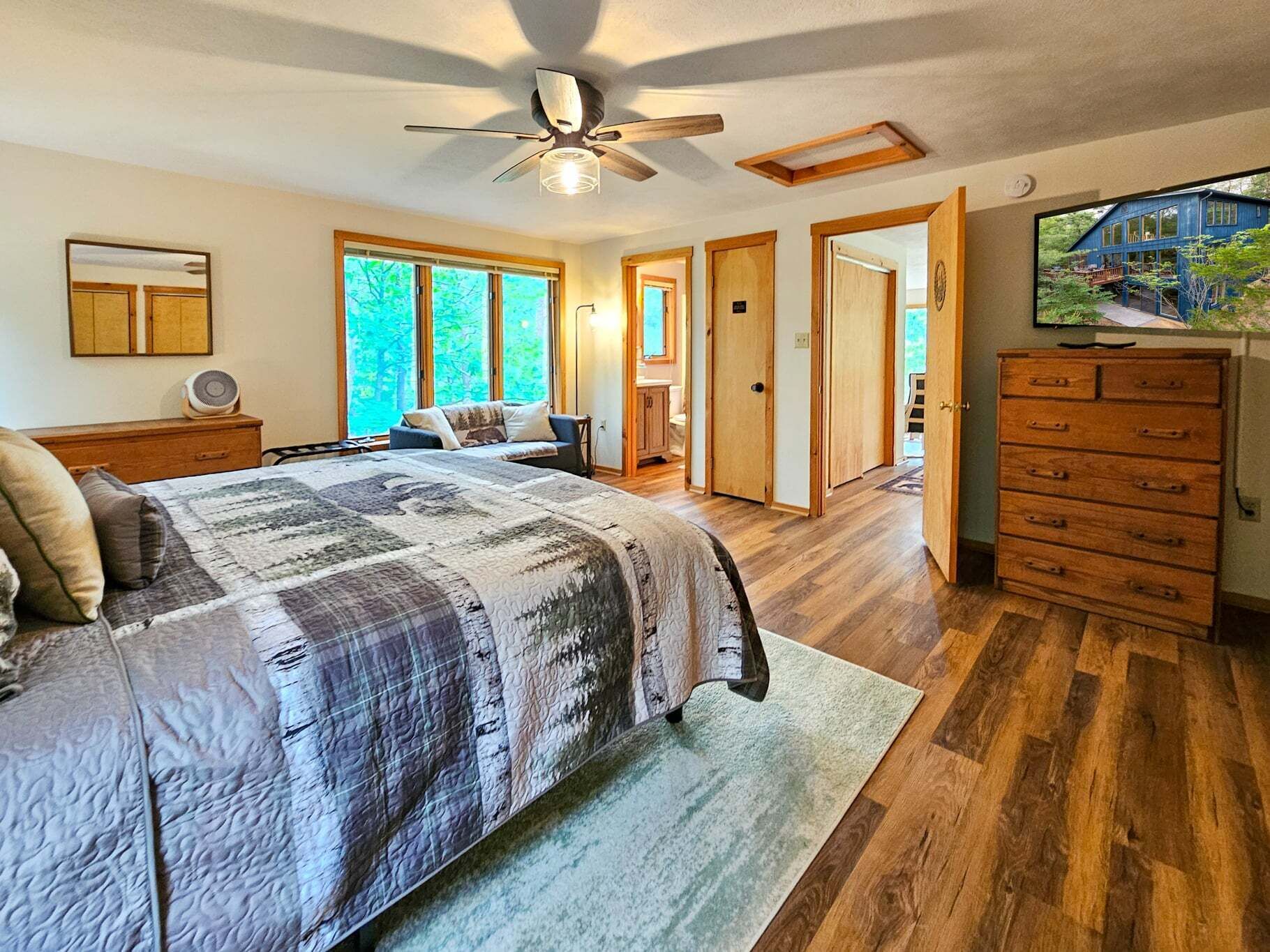 A bedroom with a large bed, a ceiling fan, and a view of the outdoors through the window.