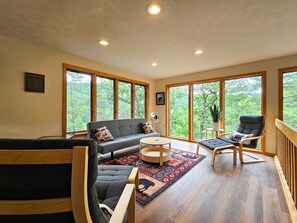 A spacious living room with a sofa, chairs, a coffee table, and large windows offering a view of the outdoors. - Bear Lodge - Hot tub & Bryce Mountain views! (Basye)