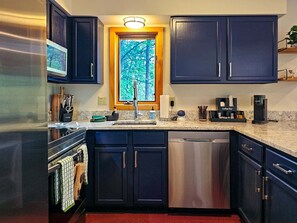A kitchen with dark cabinets, stainless steel appliances, a coffee bar, and a window with a view of trees. - Bear Lodge - Hot tub & Bryce Mountain views! (Basye)