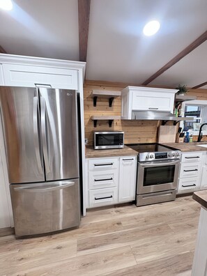 A modern kitchen with stainless steel appliances, wooden wall paneling, and white cabinetry.