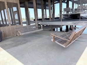 A wooden deck with a swing chair and a bench, overlooking a body of water.