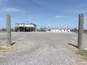 A gravel parking area with a building featuring a covered entrance and a fenced area.