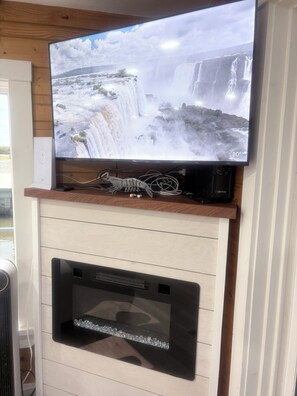 A flat-screen TV mounted on a wooden shelf above a fireplace with a decorative lobster.