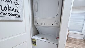 A laundry room with a white washing machine, a detergent package on top, and a sign on the wall.