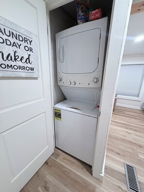 A laundry room with a white washing machine, a detergent package on top, and a sign on the wall.