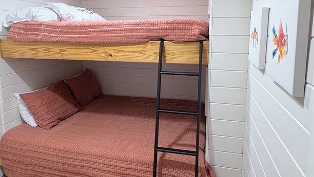 A bunk bed with a ladder, wooden headboard, and a pink bedspread.