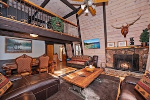 A spacious living area with a fireplace, wooden walls, and a balcony with railings. - Bearwoods Barn W Spa Near Snow Summit (Big Bear Lake)