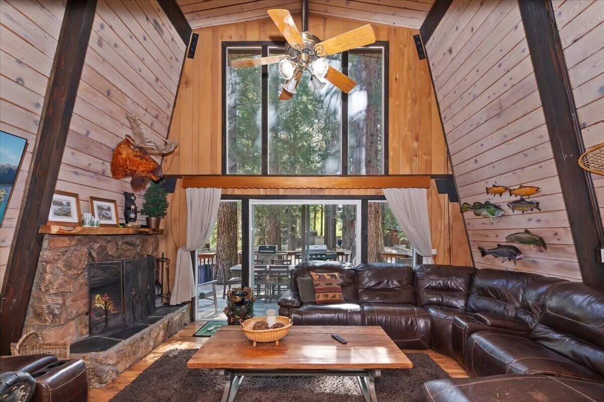 Ein gemütliches Blockhaus-Interieur mit Kamin aus Stein, Ledersofa und Deckenventilator.