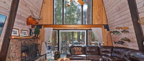L’intérieur d’un chalet chaleureux, avec une cheminée en pierre, un canapé en cuir et un ventilateur de plafond.