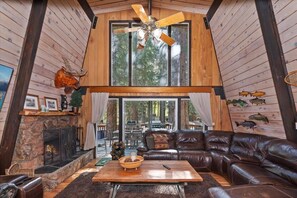 Ein gemütliches Blockhaus-Interieur mit Kamin aus Stein, Ledersofa und Deckenventilator.