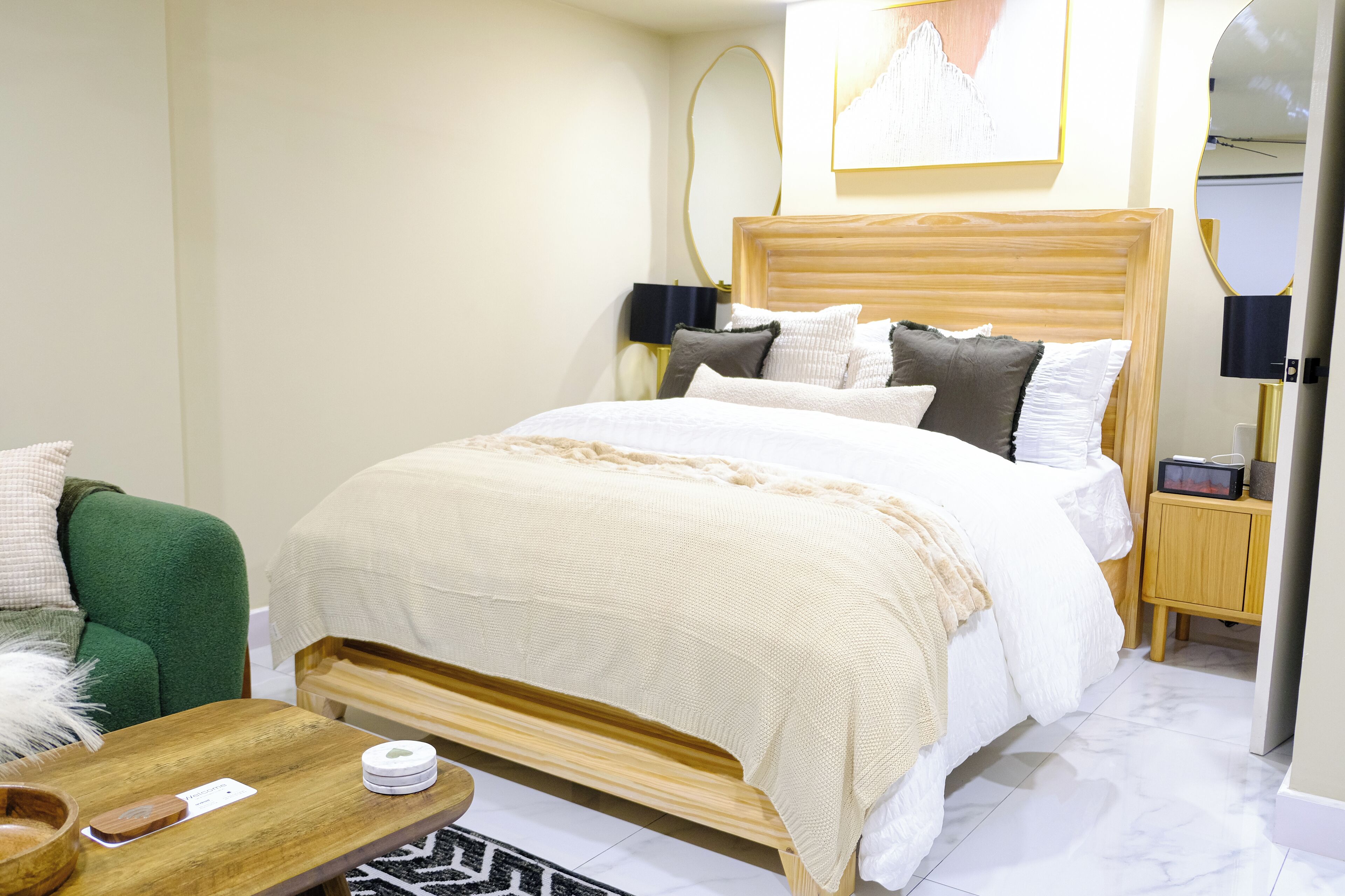 Moderni hotellihuone, jossa on suuri sänky, vihreä nojatuoli, puinen sivupöytä ja pieni yöpöytä, jossa on lamppu.