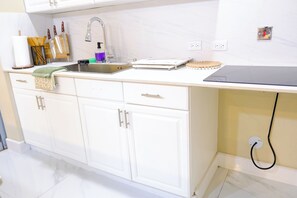 A kitchen with white cabinets, a stainless steel sink, and a countertop with various items. - Walk to the Beach Ocho Rios Apartment (Ocho Rios)