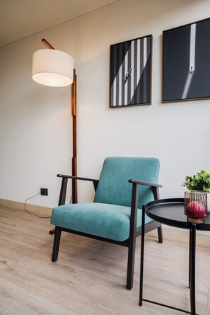 Ein modernes Zimmer mit einem moosgrünen Polsterstuhl, einem runden Tisch und einem roten Gegenstand sowie einer Stehlampe.